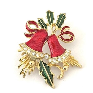May include: A gold-tone metal brooch featuring two red enamelled bells with clear rhinestone accents along the rims. The design includes green enamelled holly leaves and a red ribbon bow, with gold-tone metal sprigs extending from the base of the bells.
