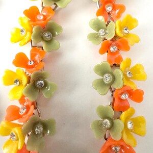 May include: A pair of long drop earrings featuring a vertical arrangement of small, multi-colored flowers in shades of orange, yellow, and sage green. Each individual flower petal is accented with a small, clear, sparkling rhinestone at the center.