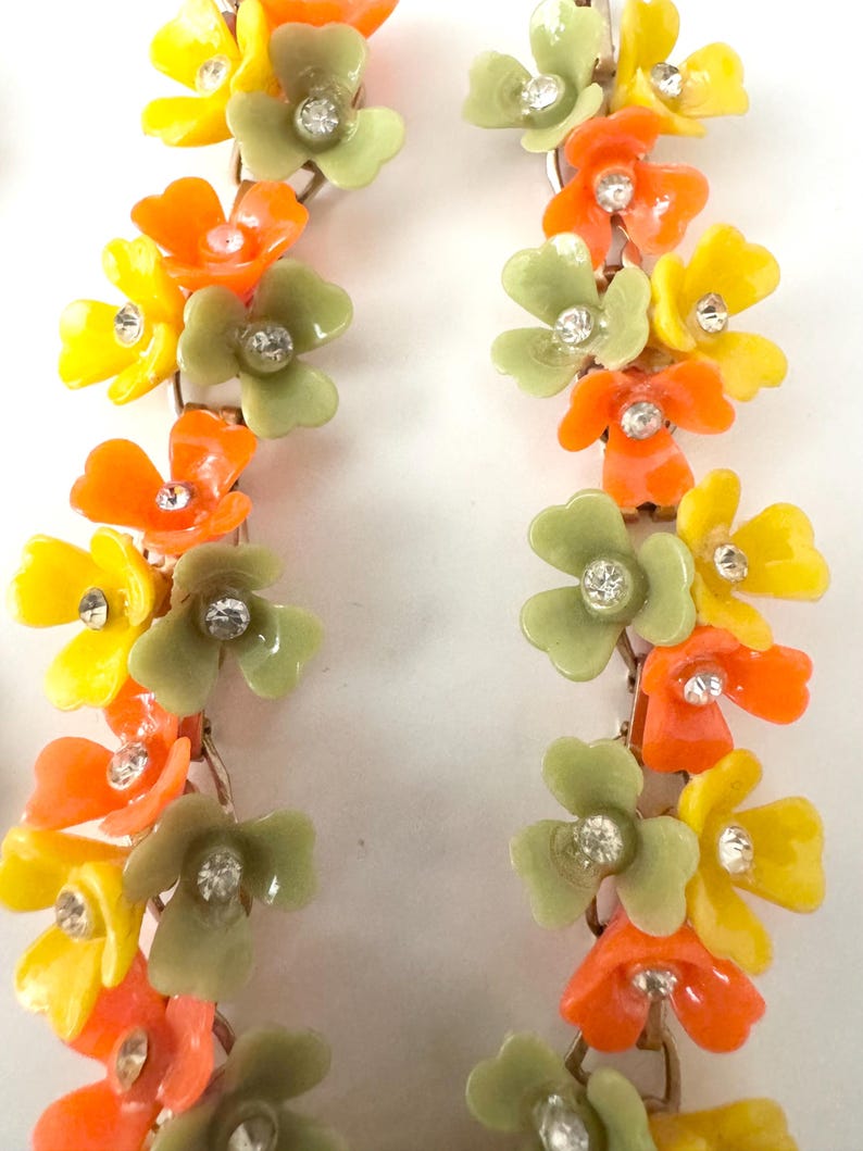 May include: A pair of long drop earrings featuring a vertical arrangement of small, multi-colored flowers in shades of orange, yellow, and sage green. Each individual flower petal is accented with a small, clear, sparkling rhinestone at the center.