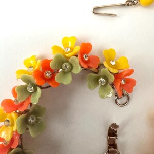 May include: A floral bracelet and matching earring set featuring yellow, orange, and sage green plastic flower charms. Each flower is accented with a small, clear, round rhinestone at the center. The bracelet has a metal clasp and link chain.