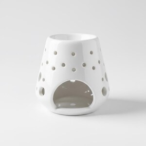 Puede incluir: Un difusor de aceites esenciales de cerámica blanca con acabado brillante. El difusor tiene forma redondeada con numerosos agujeros pequeños y espaciados uniformemente y una gran abertura en la base. Está diseñado para aromaterapia.