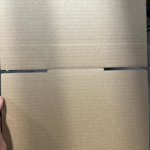 May include: A partially assembled, unfolded cardboard box. The box is made of corrugated cardboard and has a natural brown color. The top flaps are open, revealing the interior. The box is likely used for shipping or storage.