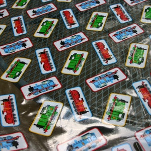 May include: Rectangular patches featuring cartoon train illustrations in red, green, and blue. Each patch has a white border and a yellow outline. The patches are scattered across a reflective surface, creating a playful pattern.