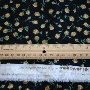 May include: Black fabric with a small yellow rose print. A ruler is placed on top of the fabric, and a white label with the text "TP1074 Original Cotton Lawn Design by makower uk © ENGLAND" is below the ruler.