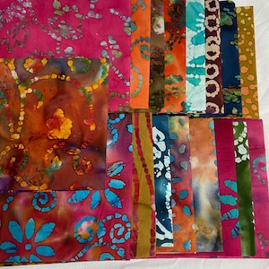 May include: A collection of 20 fabric squares in various shades of pink, orange, brown, blue, and green. The fabric squares feature a batik design with swirling patterns and floral motifs.