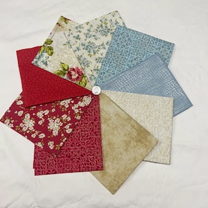 May include: A collection of fabric squares arranged in a circular pattern. The fabrics feature floral, paisley, and textured designs in shades of red, blue, cream, and tan. A coin is in the center of the arrangement.