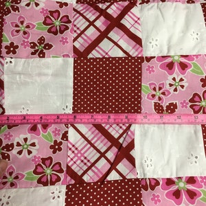 May include: A patchwork quilt with squares of different fabrics. The fabrics are pink, white, and red with various patterns including polka dots, plaid, and floral designs.