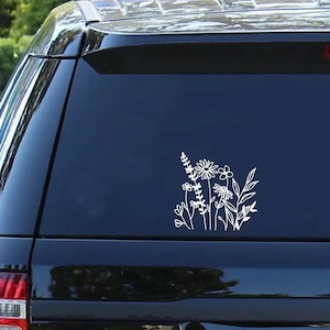 May include: A white vinyl decal featuring a line art illustration of a wildflower bouquet with various stems, leaves, and blossoms. The sticker is applied to the dark tinted rear window of a black vehicle, displaying a clean and simple botanical design.
