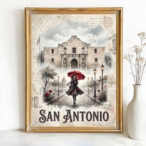 May include: Framed art print featuring a watercolor illustration of the Alamo in San Antonio, Texas. A person with a red umbrella walks on a cobblestone path. The print includes the text "San Antonio" in a decorative font, with a gold frame.