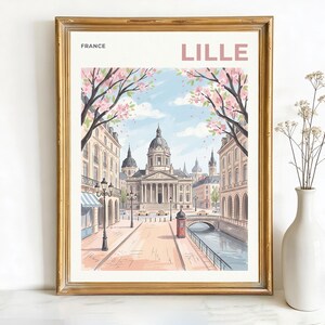 May include: A framed print of Lille, France, featuring a watercolor illustration of a city street with buildings, a bridge, and a canal. The artwork includes pink flowering trees, a red phone booth, and the word "LILLE" in pink.