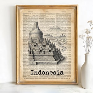 May include: Framed print featuring a black and white illustration of a temple and mountain landscape. The artwork is set against a vintage dictionary page background. The word "Indonesia" is printed in a bold, black font at the bottom of the image. The frame is gold.