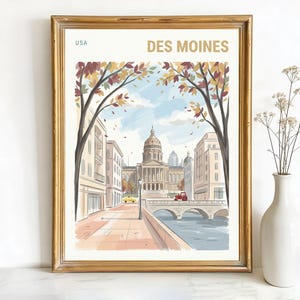 May include: A framed art print showing a watercolour illustration of Des Moines, Iowa. The artwork depicts a city street scene with a domed building, bridge, and autumn foliage. The print is in a gold frame and includes the text "DES MOINES" and "USA".