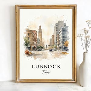 May include: Watercolor print of Lubbock, Texas, in a gold frame. The artwork depicts a street scene with buildings, a clock tower, and cars. The word "Lubbock" and "Texas" are written in black script at the bottom of the print.