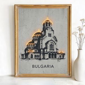May include: Framed art print featuring a grayscale illustration of a cathedral with illuminated gold accents. The word "BULGARIA" is printed in a bold font at the bottom. The artwork is in a gold frame.