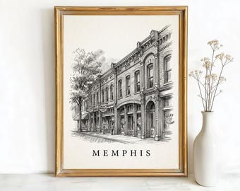 May include: A framed black and white sketch depicting a street scene in Memphis. The artwork shows detailed drawings of buildings, shops, and a tree. The word "MEMPHIS" is printed in a bold font at the bottom. The frame is gold.