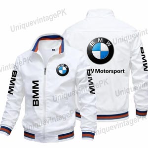 Pode incluir: Casaco branco com zíper com o logotipo da BMW no peito e nas costas, e "BMW" impresso nas mangas. O casaco tem listras azuis, laranja e azul marinho na gola, punhos e bainha. O texto "BMW Motorsport" é impresso nas costas.