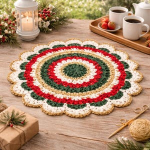 May include: A round, crocheted placemat with a scalloped edge. The design features concentric circles of red, green, white, and gold. The placemat is on a wooden table, with a candle lantern, coffee cups, and a gift box in the background.