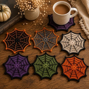 May include: A set of seven crocheted spider web coasters in various colors including black with orange, grey with orange, cream with black, purple with black, green with black, and solid orange with black, with one coaster holding a coffee mug.