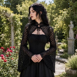 May include: A black crochet bolero with long flared sleeves and a high neck featuring a tie closure, worn over a black strapless bodice and a long black skirt. The bolero has an open-knit pattern with scalloped edges along the sleeve cuffs.