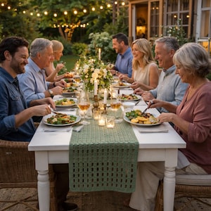 Op de afbeelding: Een groep mensen dineert buiten aan een witte tafel. De tafel is gedekt met borden eten, wijnglazen, kaarsen en een groene tafelloper. Boven de tafel hangen lichtslingers, die een warme en uitnodigende sfeer creëren.