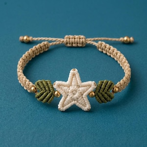 May include: Macrame bracelet featuring a cream-colored star, olive green accents, and gold beads. The adjustable bracelet is made of beige macrame cord. A handcrafted, bohemian style accessory.