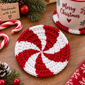 May include: A round crochet coaster featuring a red and white spiral peppermint candy pattern. The coaster is crafted with yarn in a circular design, alternating between red and white segments that radiate from the center to the outer edge.