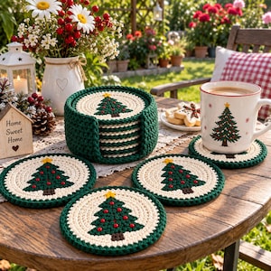 May include: A set of round, crocheted coasters featuring a green Christmas tree design with a yellow star topper and red ornaments on a cream background, stacked in a matching dark green holder, with one coaster placed under a white ceramic mug.