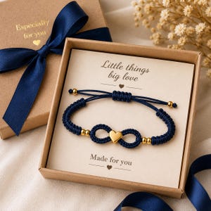 May include: A navy blue bracelet with a gold heart charm and gold beads, presented in a gift box with a navy blue ribbon. The box reads "Especially for you" and the card inside says "Little things big love."