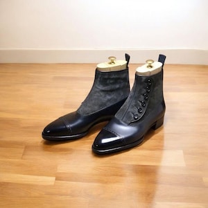 Puede incluir: Un par de botines de cuero negro con puntera. Las botas tienen un panel de ante gris en la parte superior y se abrochan con botones. Hormas de madera dentro de las botas.