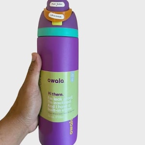 May include: A purple Owala water bottle with a teal collar and a multi-colored lid featuring a push button and lift to unlock mechanism. The bottle has a green label with the text Hi there. I'm leak proof. I'm insulated. And I have a built-in straw. 24 oz./710ml.