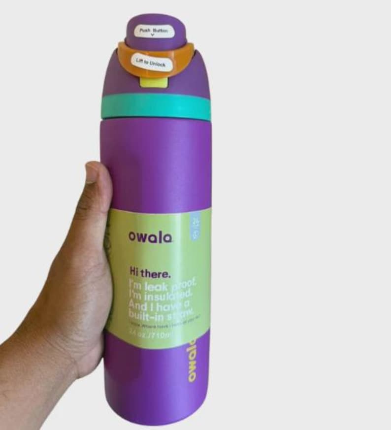 May include: A purple Owala water bottle with a teal collar and a multi-colored lid featuring a push button and lift to unlock mechanism. The bottle has a green label with the text Hi there. I'm leak proof. I'm insulated. And I have a built-in straw. 24 oz./710ml.