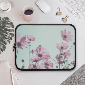 Könnte beinhalten: Eine rechteckige Laptoptasche mit einem Druckdesign aus hellrosa Kosmosblüten auf einem blass mintgrünen Hintergrund. Die Tasche hat einen schwarzen Reißverschlussrand und eine weich gepolsterte Außenseite als Schutzhülle.