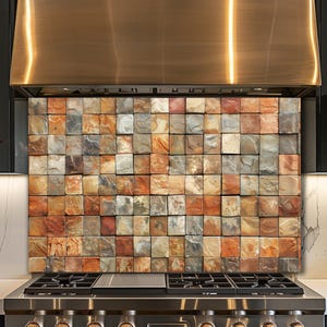 Op de afbeelding: Een keukenachterwand met een mozaïek van vierkante tegels in bruin, oranje, grijs en rood. De tegels hebben een textuur die op steen lijkt. De achterwand is geïnstalleerd boven een roestvrijstalen gasfornuis.