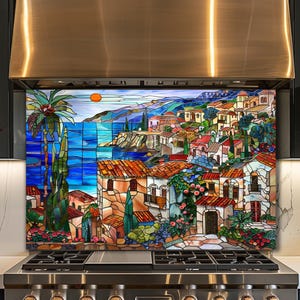 Op de afbeelding: Een rechthoekig keukenachterwandpaneel met een illustratie in glas-in-loodstijl van een mediterraan kustdorp. De scène toont gebouwen met terracotta daken, een felblauwe zee, een palmboom en een kleine oranje zon aan de hemel.