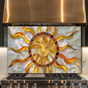 May include: A stained glass sun design backsplash with a smiling face at the center. The sun features yellow, orange, and brown hues, with a white background. The backsplash is installed above a stainless steel stove.