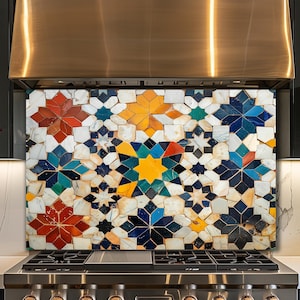 May include: A kitchen backsplash featuring a geometric mosaic tile pattern with star and polygon shapes in shades of red, yellow, blue, green, and white, positioned behind a stainless steel gas stove and a large metallic range hood.