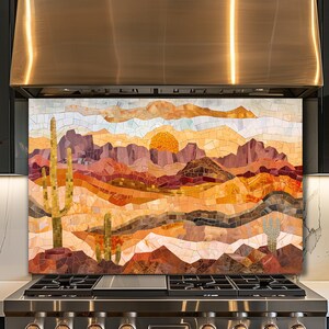 May include: A mosaic backsplash depicting a desert landscape with a setting sun. The artwork features a color palette of warm oranges, browns, and yellows, with cacti and mountains. The mosaic is installed above a stainless steel stove.