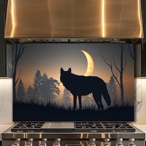Puede incluir: Silueta negra de un lobo frente a un bosque y una luna creciente. El fondo presenta un degradado naranja y gris, con árboles y hierba silueteados. Esta obra de arte es probablemente un protector de salpicaduras de cocina decorativo.