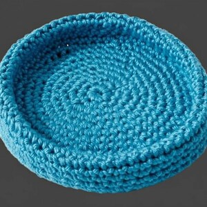Peut inclure: Un panier rond en crochet turquoise. Le panier est fabriqué avec de la grosse laine et présente un motif en spirale au centre. Les côtés sont légèrement relevés, créant une forme de bol. Idéal pour ranger de petits objets.