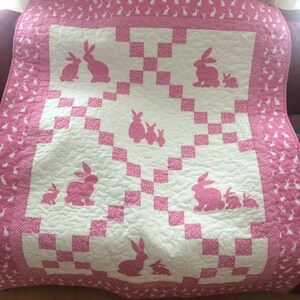 May include: A pink and white quilt with a checkered pattern and a repeating design of pink bunny silhouettes.
