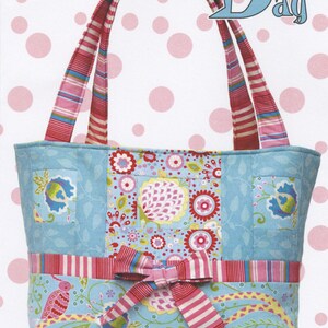 May include: A blue and pink tote bag with a bow on the front. The bag has a floral print and a striped handle. The text "The Bow Bag" is in blue letters on a white background. The text "Cool Cat Creations" and "CCC 101" are at the bottom of the image.