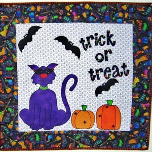 May include: A purple cat with a black mask sits in front of a white background with the text "trick or treat" in black letters. Two orange pumpkins with black spiderwebs are on either side of the cat. The background is a black and white pattern with various Halloween-themed images.