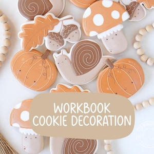 Peut inclure: Une collection de biscuits au sucre sur le thème de l'automne en forme de citrouilles, escargots, champignons, glands et feuilles de chêne, décorés de glaçage. Un encart rectangulaire beige porte le texte blanc WORKBOOK COOKIE DECORATION.