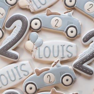 Può includere: Un assortimento di biscotti di zucchero decorati, tra cui auto da corsa azzurre con il numero 2, biscotti con il numero 2 con un design stradale e biscotti con il nome "LOUIS". Alcuni biscotti hanno piccole decorazioni a palloncino. I biscotti sono in una palette di colori chiari.