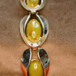 May include: A vintage bracelet featuring three oval, olive-green cabochon stones set in silver-tone metal. The bracelet has a classic design with a polished finish, suitable for adding a touch of retro style to any outfit.