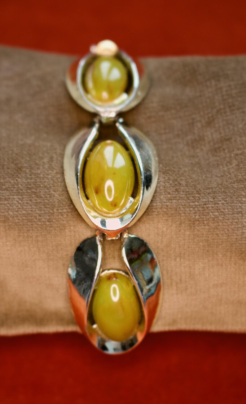 May include: A vintage bracelet featuring three oval, olive-green cabochon stones set in silver-tone metal. The bracelet has a classic design with a polished finish, suitable for adding a touch of retro style to any outfit.