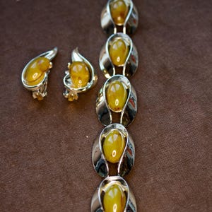 May include: A vintage jewelry set featuring a bracelet and two earrings. The bracelet and earrings have a silver-tone metal setting with oval-shaped, amber-colored stones. The earrings are clip-on style.