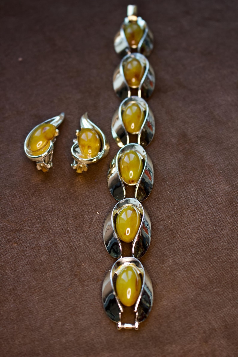May include: A vintage jewelry set featuring a bracelet and two earrings. The bracelet and earrings have a silver-tone metal setting with oval-shaped, amber-colored stones. The earrings are clip-on style.