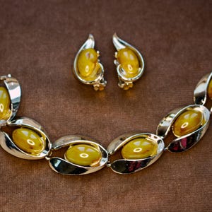 May include: A vintage jewelry set featuring a bracelet and matching earrings. The set has a silver-tone metal setting with oval-shaped, amber-colored stones. The bracelet is composed of linked ovals, and the earrings are clip-ons.