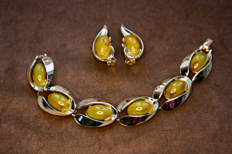 May include: A vintage jewelry set featuring a bracelet and matching earrings. The set has a silver-tone metal setting with oval-shaped, amber-colored stones. The bracelet is composed of linked ovals, and the earrings are clip-ons.